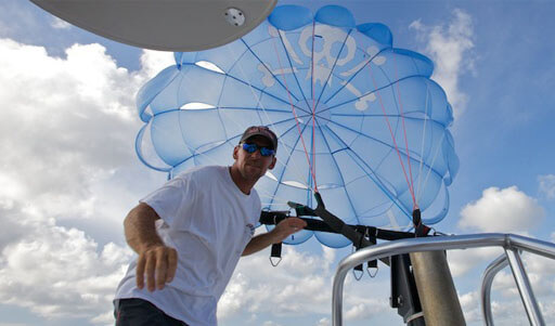 A high-angle shot of a man under a blue parasail wing with a pirate skull printed on it.